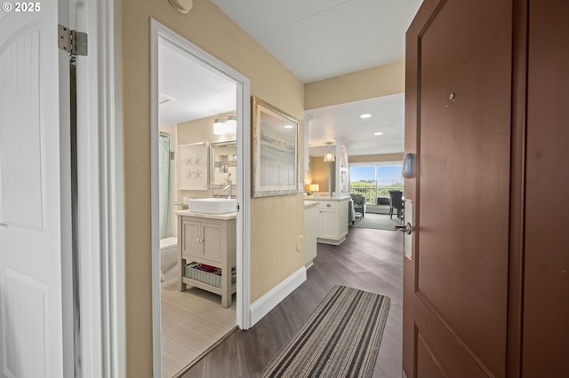 corridor with dark wood-style floors, recessed lighting, a sink, and baseboards