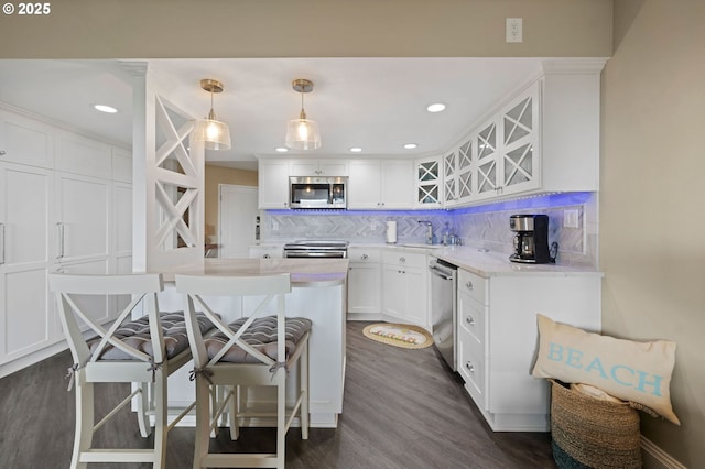 kitchen with a breakfast bar, stainless steel appliances, backsplash, dark wood-type flooring, and white cabinetry