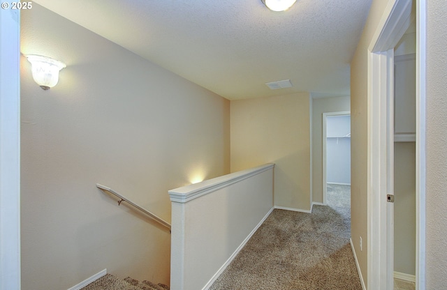 hall with light carpet, baseboards, a textured ceiling, and an upstairs landing