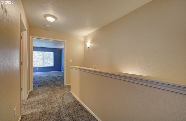 corridor featuring light carpet, a textured ceiling, and baseboards