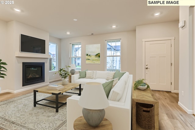 living room with baseboards, light wood-style floors, a glass covered fireplace, and recessed lighting