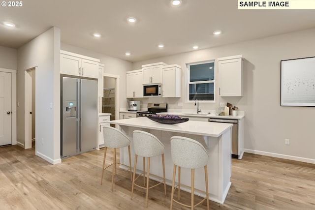 kitchen with stainless steel appliances, sink, white cabinetry, light hardwood / wood-style flooring, and a kitchen island