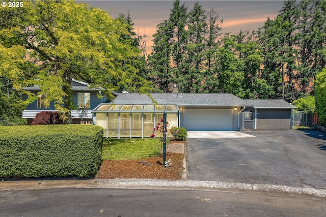 view of front of home with aphalt driveway, a shingled roof, an exterior structure, an attached garage, and an outdoor structure