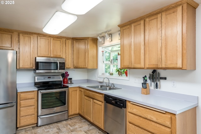 kitchen with appliances with stainless steel finishes, a sink, stone finish flooring, light countertops, and track lighting