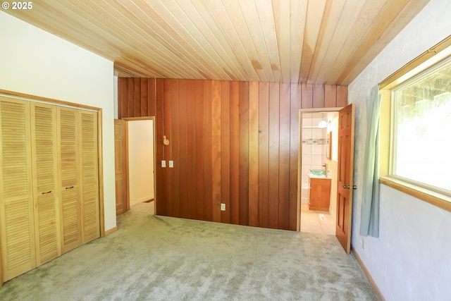 unfurnished bedroom with carpet, a closet, wood ceiling, wooden walls, and connected bathroom