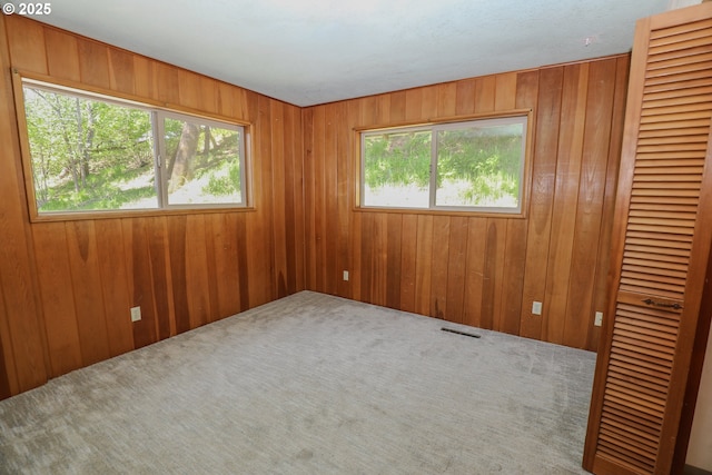 unfurnished room with wooden walls, carpet flooring, and visible vents