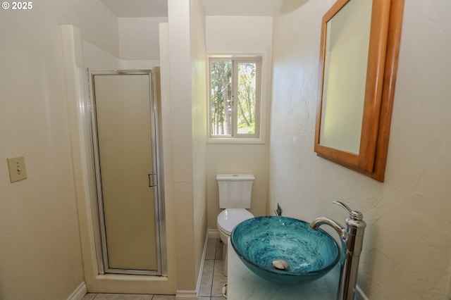 bathroom featuring toilet, tile patterned floors, a sink, a stall shower, and baseboards