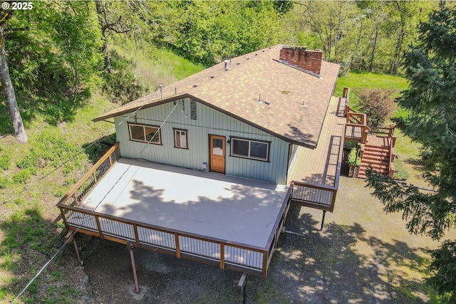 rear view of house with a chimney, a shingled roof, stairs, a deck, and a forest view