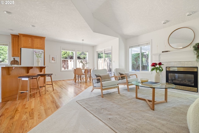 living room with a textured ceiling, light wood-style flooring, healthy amount of natural light, a tile fireplace, and baseboards