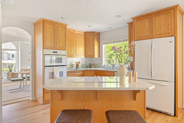 kitchen with white appliances, light wood finished floors, a sink, a breakfast bar, and a center island