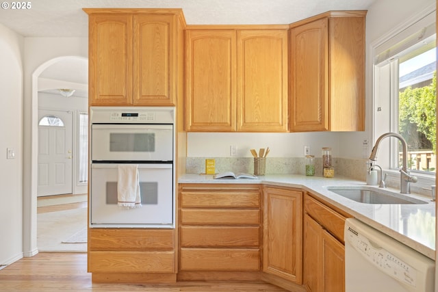 kitchen featuring white appliances, a sink, light wood-type flooring, and arched walkways