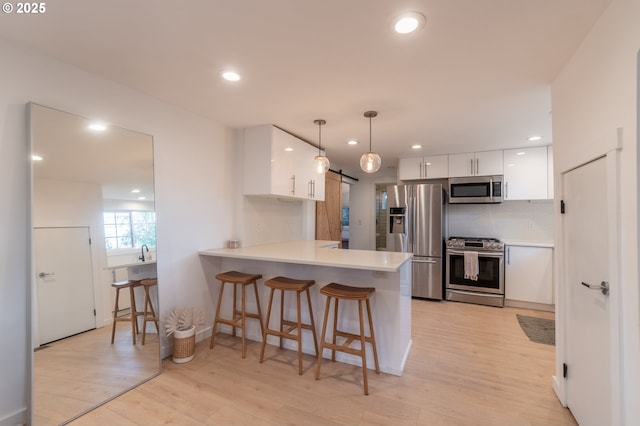 kitchen with stainless steel appliances, a peninsula, white cabinetry, a breakfast bar area, and light countertops