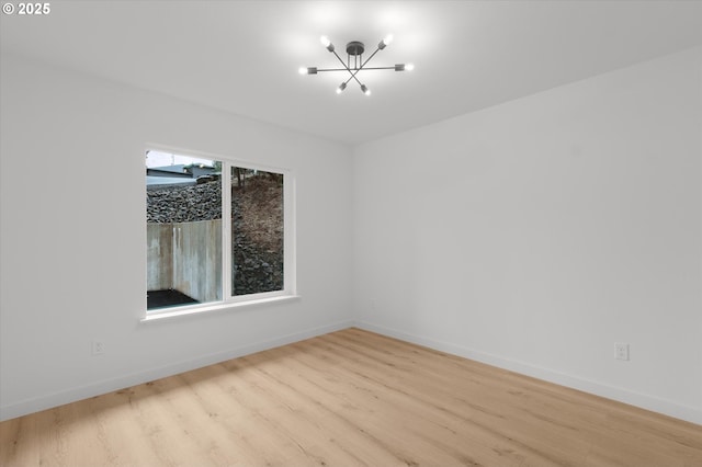 spare room with a chandelier and light wood-type flooring