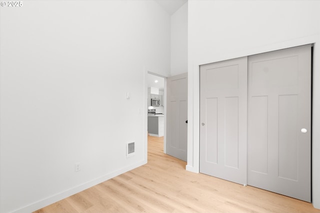 unfurnished bedroom featuring a closet, a high ceiling, and light wood-type flooring