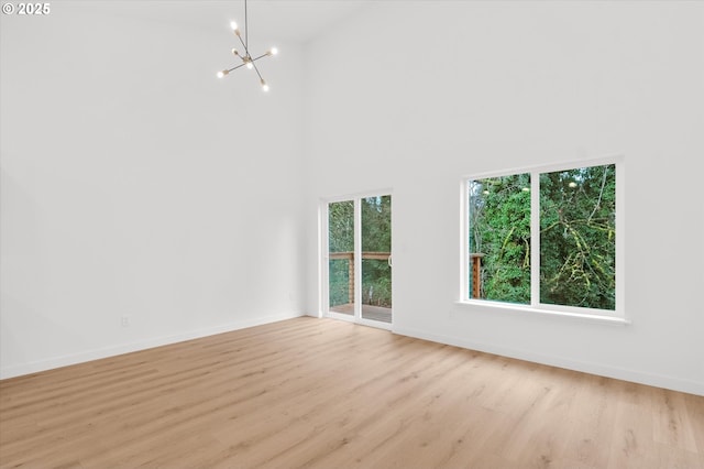 unfurnished living room featuring a towering ceiling, an inviting chandelier, and light hardwood / wood-style flooring