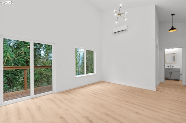 unfurnished living room featuring a towering ceiling, a wall mounted air conditioner, sink, a notable chandelier, and light hardwood / wood-style floors