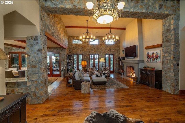 23021 Brushline Ct, Bend, OR 97701 - living room featuring hardwood / wood-style flooring, beamed ceiling, a high ceiling, a chandelier, and a warm lit fireplace
