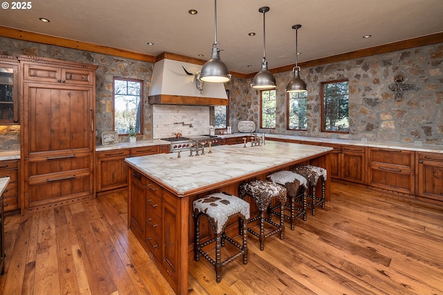 23021 Brushline Ct, Bend, OR 97701 - kitchen featuring brown cabinets, custom exhaust hood, light wood-type flooring, a center island with sink, and a kitchen breakfast bar