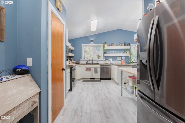 kitchen with lofted ceiling, sink, appliances with stainless steel finishes, white cabinetry, and light wood-type flooring