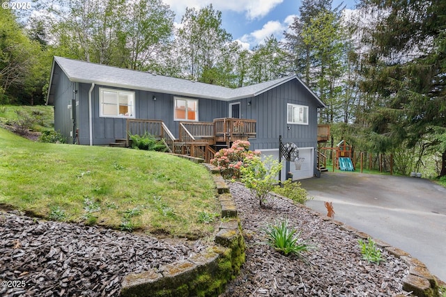 view of front of home with a garage, a deck, a playground, and a front lawn