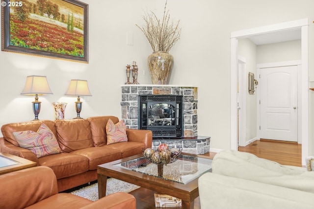 living area featuring a stone fireplace, baseboards, and wood finished floors