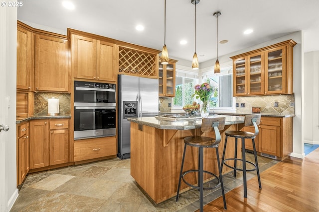 kitchen featuring brown cabinetry, a kitchen island, appliances with stainless steel finishes, a breakfast bar, and glass insert cabinets