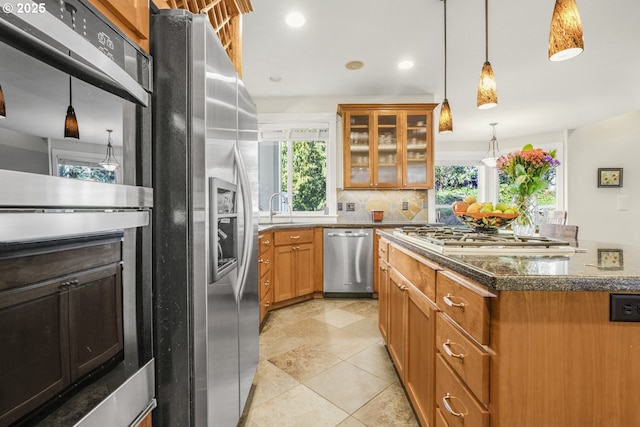 kitchen featuring decorative backsplash, dark stone counters, glass insert cabinets, appliances with stainless steel finishes, and a sink