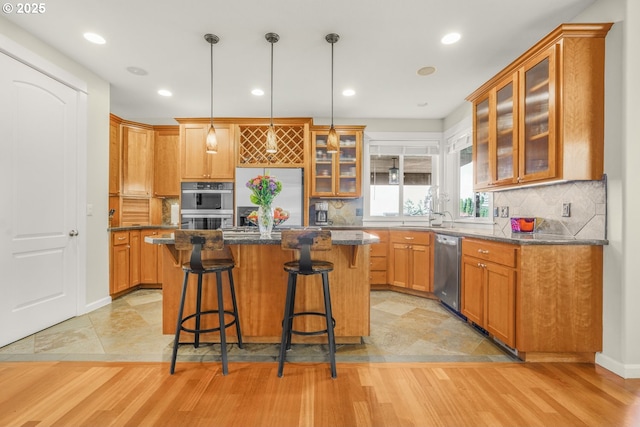 kitchen featuring a breakfast bar area, stainless steel appliances, light wood-style floors, a center island, and dark stone countertops