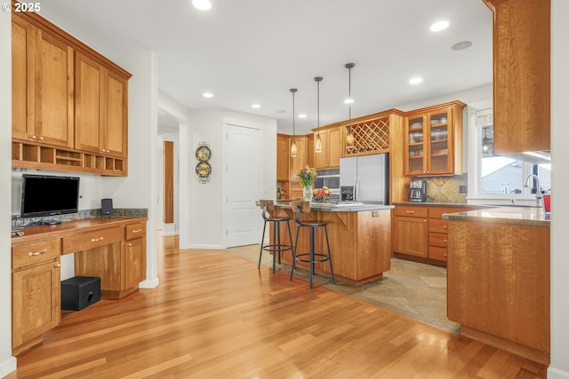 kitchen with stainless steel refrigerator with ice dispenser, a breakfast bar area, light wood-style floors, a sink, and a kitchen island