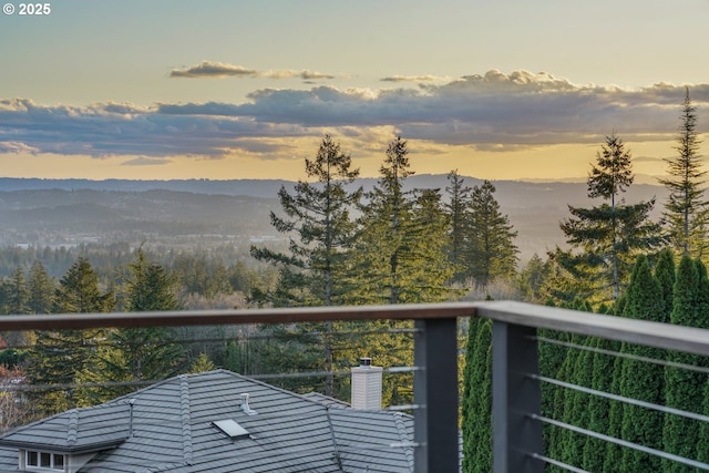 balcony at dusk featuring a mountain view and a view of trees