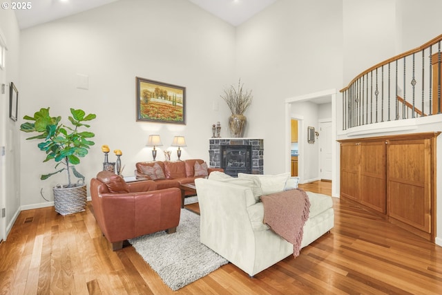 living room featuring a fireplace, a towering ceiling, light wood-style flooring, and baseboards