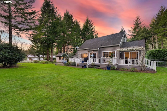 back house at dusk featuring a lawn, an outdoor structure, and a deck