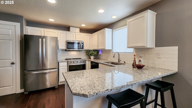 kitchen featuring a peninsula, light stone counters, stainless steel appliances, and a sink