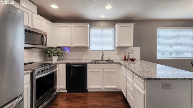 kitchen with appliances with stainless steel finishes, dark wood-style flooring, a peninsula, white cabinetry, and a sink