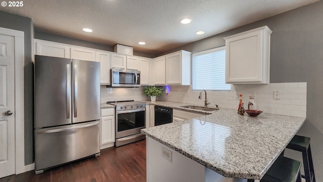 kitchen featuring light stone counters, dark wood finished floors, appliances with stainless steel finishes, a sink, and a peninsula