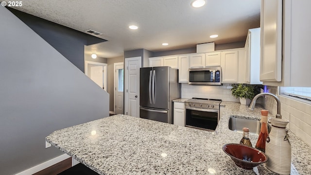 kitchen featuring a peninsula, a sink, appliances with stainless steel finishes, backsplash, and light stone countertops