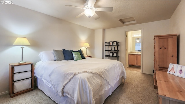 bedroom with attic access, light carpet, connected bathroom, a textured ceiling, and ceiling fan