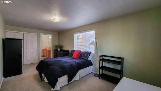 bedroom featuring light colored carpet, a textured ceiling, and ensuite bath