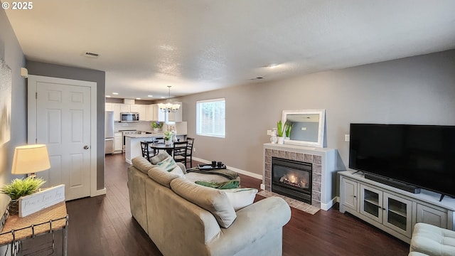 living room with dark wood-style floors, a tile fireplace, visible vents, and baseboards