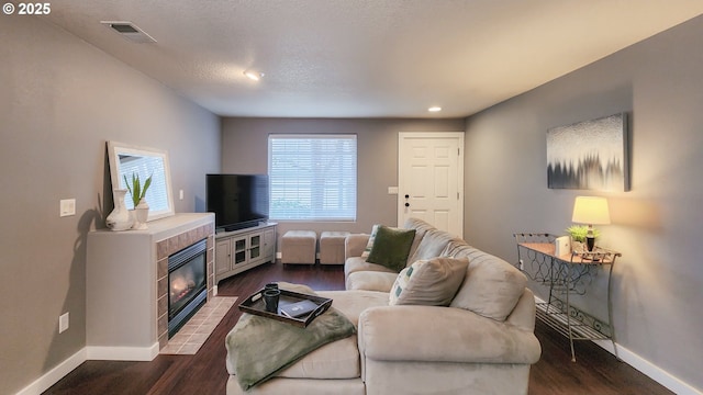 living room featuring a tile fireplace, visible vents, dark wood finished floors, and baseboards