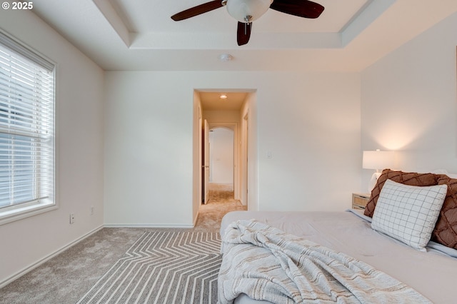 carpeted bedroom with ceiling fan and a raised ceiling