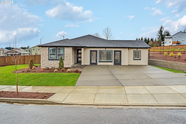 view of front of home featuring roof with shingles, fence, concrete driveway, and a front yard