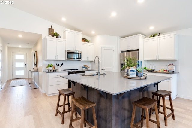 kitchen featuring white cabinets, appliances with stainless steel finishes, a kitchen breakfast bar, light wood-style floors, and a sink