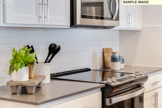 kitchen with decorative backsplash, stainless steel microwave, light countertops, white cabinetry, and range with electric stovetop