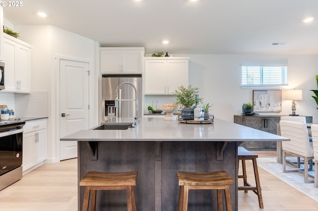 kitchen with visible vents, a breakfast bar area, stainless steel appliances, white cabinetry, and backsplash