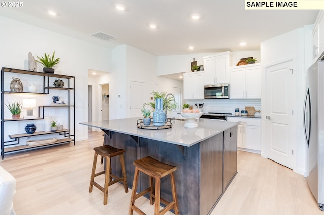 kitchen featuring visible vents, appliances with stainless steel finishes, light wood-type flooring, a kitchen bar, and white cabinetry