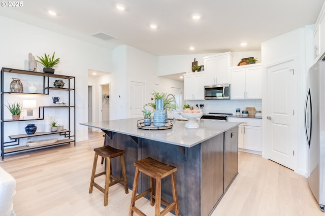 kitchen featuring a breakfast bar, visible vents, white cabinets, appliances with stainless steel finishes, and light wood-type flooring