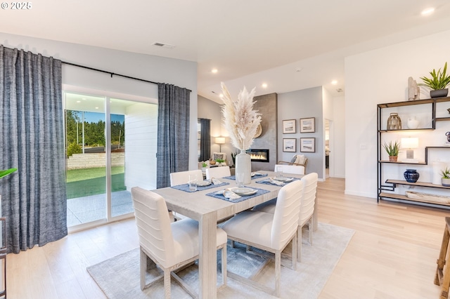 dining space featuring vaulted ceiling, a large fireplace, light wood finished floors, and visible vents