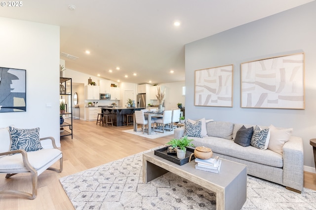 living area with baseboards, visible vents, vaulted ceiling, light wood-type flooring, and recessed lighting