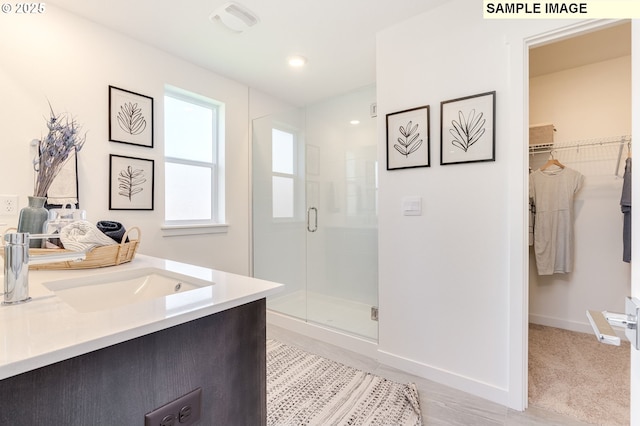 full bath featuring a stall shower, visible vents, baseboards, a walk in closet, and vanity